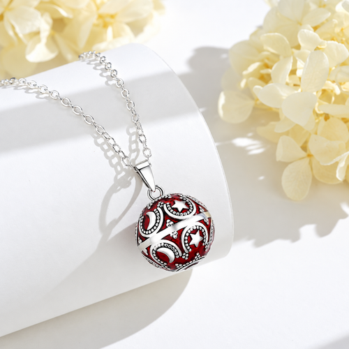Collier bola Amaya rouge et argenté posé sur un support blanc, fleurs claires en décor