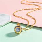 Collier bola Aurore doré et bleu posé sur fond rose et vert d’eau