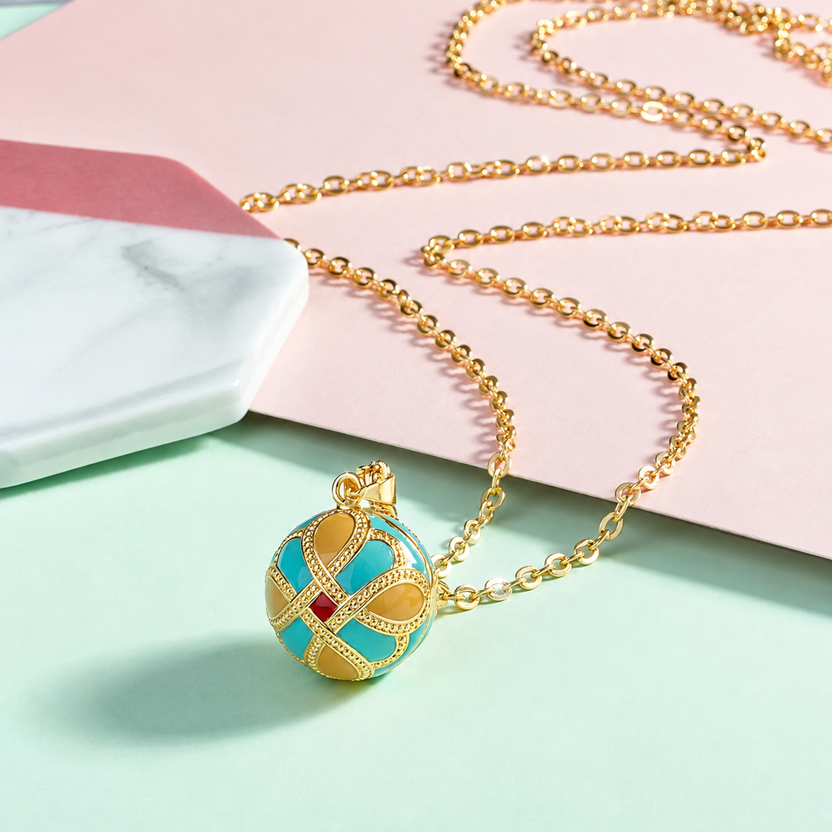 Collier bola Éternia posé sur fond rose et vert d’eau
