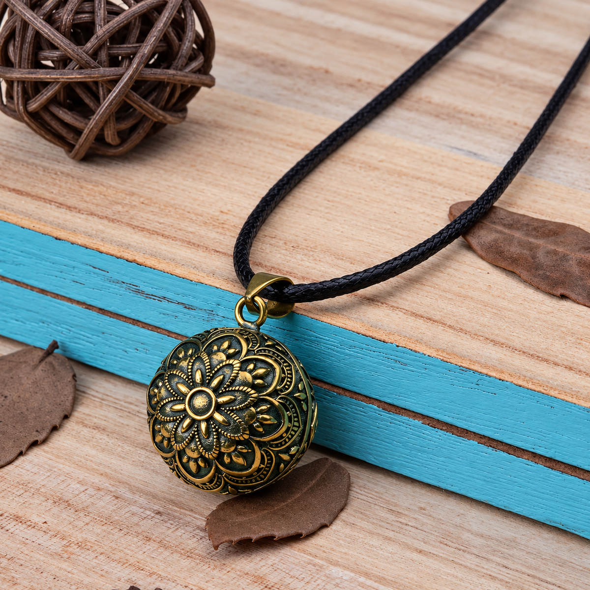 Bola Gaïa sur cordon noir posé sur un bois clair, feuilles sèches en décor