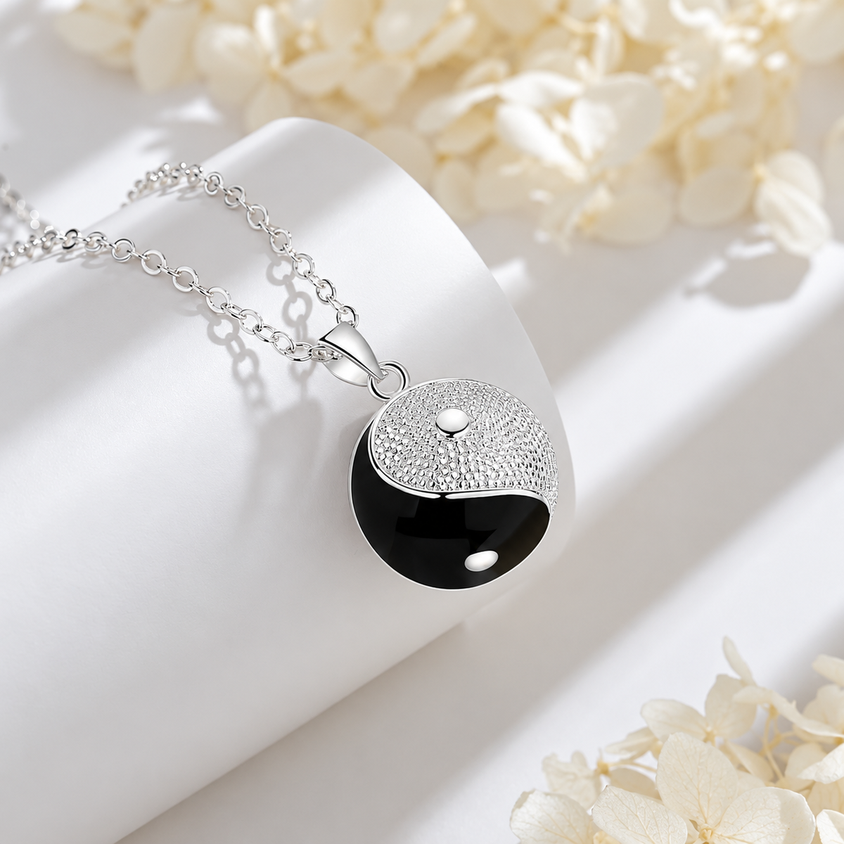 Collier bola Harmya posé sur un support blanc, fleurs claires en décor