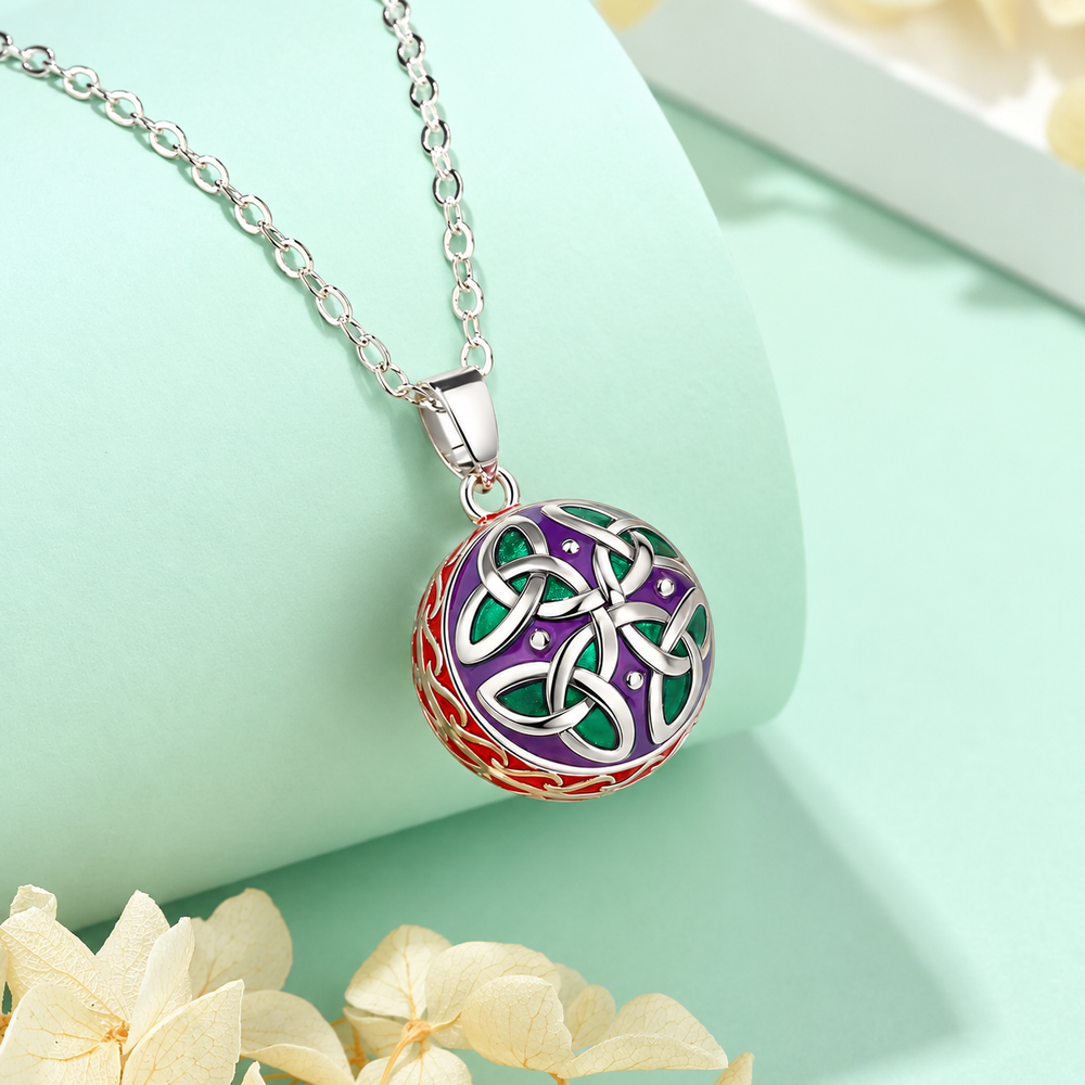 Collier bola Liéna posé sur un support vert d’eau, fleurs claires en décor