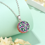 Collier bola Liéna posé sur un support vert d’eau, fleurs claires en décor
