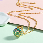 Collier bola Liora posé sur fond rose et vert d’eau