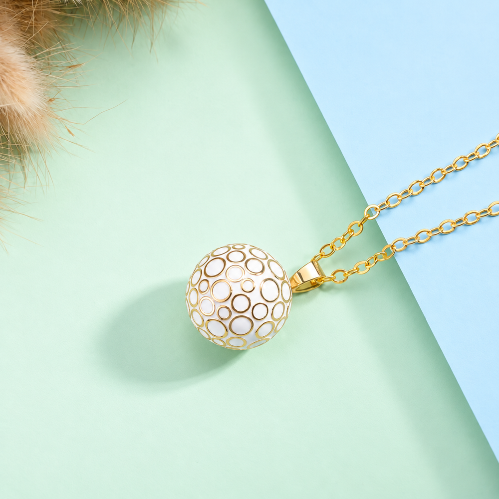 Collier bola Lunaé blanc et doré posé sur fond vert d’eau