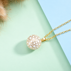 Collier bola Lunaé blanc et doré posé sur fond vert d’eau