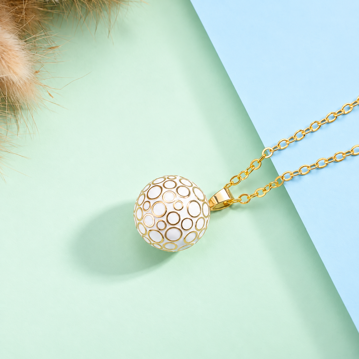 Collier bola Lunaé blanc et doré posé sur fond vert d’eau