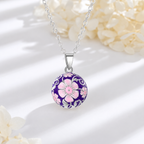 Collier bola Malia posé sur fond blanc, fleurs claires en décor