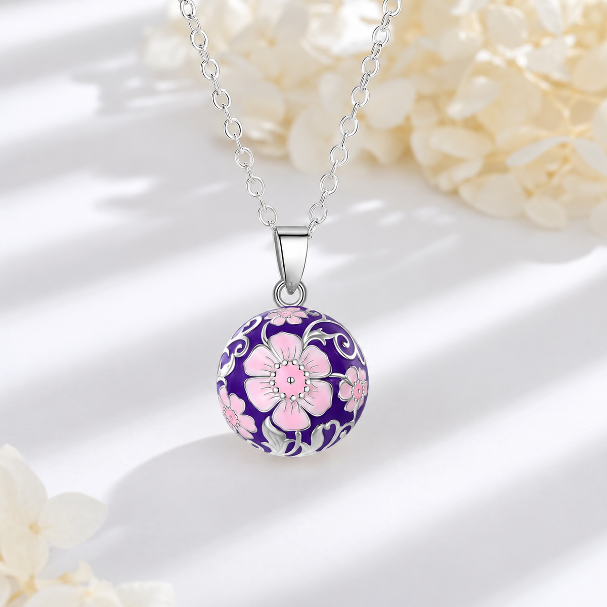 Collier bola Malia posé sur fond blanc, fleurs claires en décor