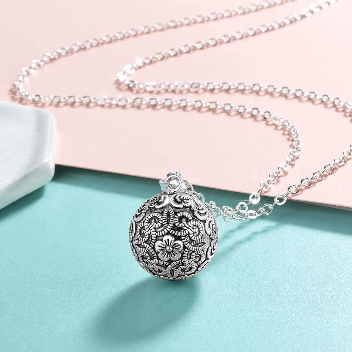 Collier bola Sélène posé sur fond rose et vert d’eau